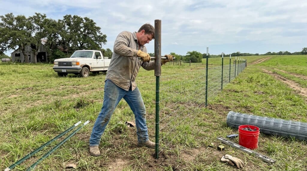Man using T-post driver to install fence post in field.
