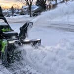 Person using a cordless snow blower to clear snow from driveway.