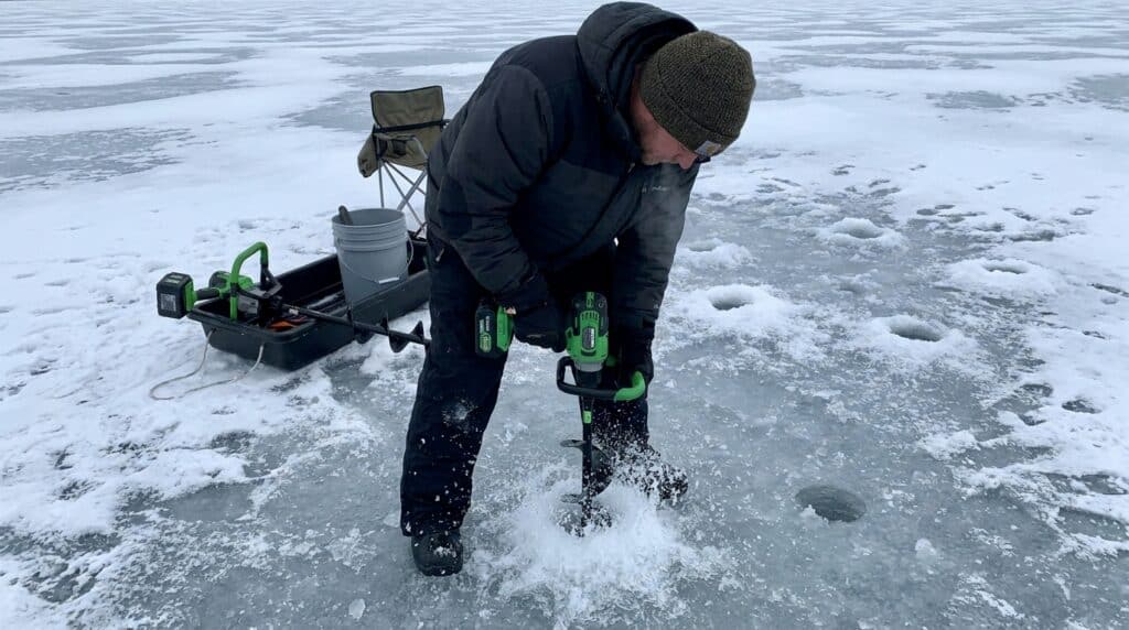 Person using cordless ice auger for ice fishing on frozen lake.