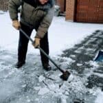 Person clearing snow with ice chopper and sidewalk scraper tools.