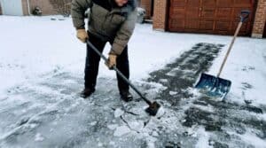 Person clearing snow with ice chopper and sidewalk scraper tools.