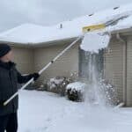 Person using snow rake to clear snow from roof in winter.