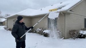 Person using snow rake to clear snow from roof in winter.