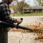 Person using leaf blower to clear leaves from driveway.
