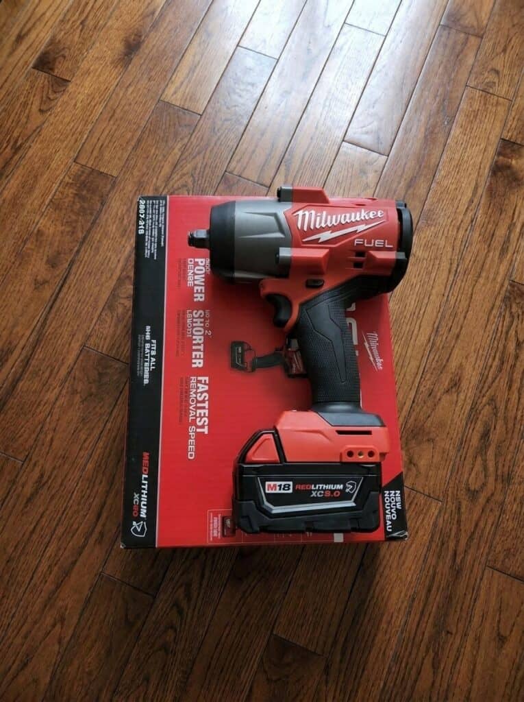 Milwaukee M18 FUEL impact wrench on red box, hardwood floor background.