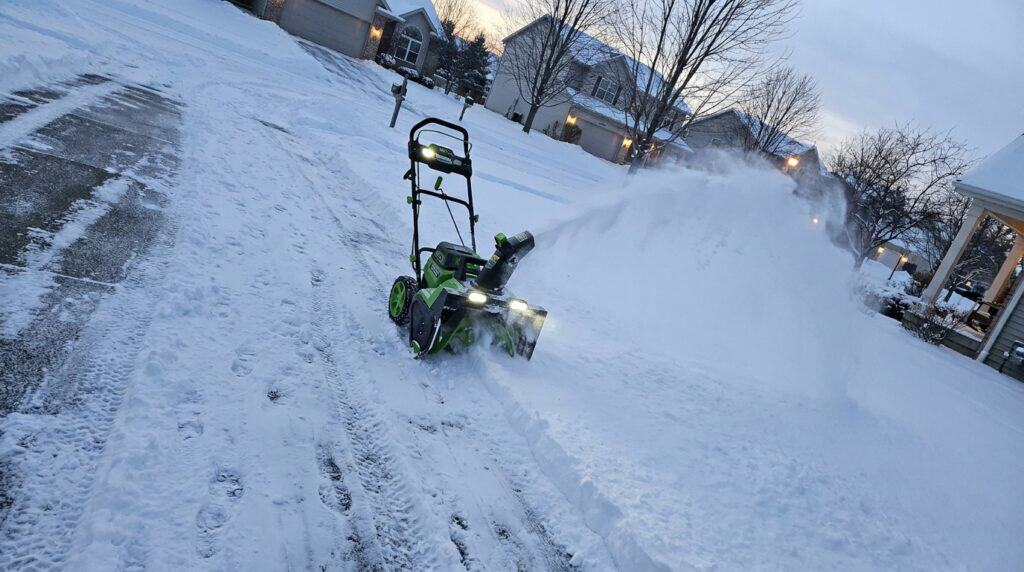 Battery-powered snow blower clearing snow from driveway in winter.