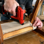 Person using a cordless staple gun on furniture upholstery project.