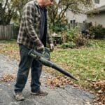 Person blowing leaves with cordless leaf blower in suburban yard.