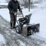 Person using snow blower on gravel driveway in winter.